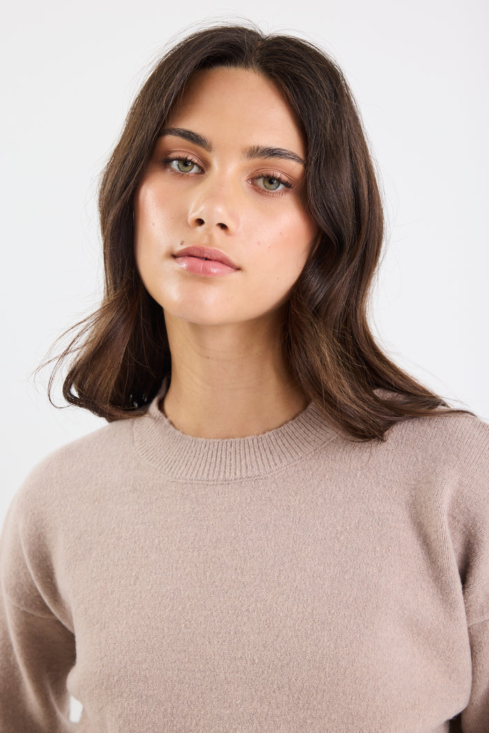 Woman wearing a beige sweater against a white background