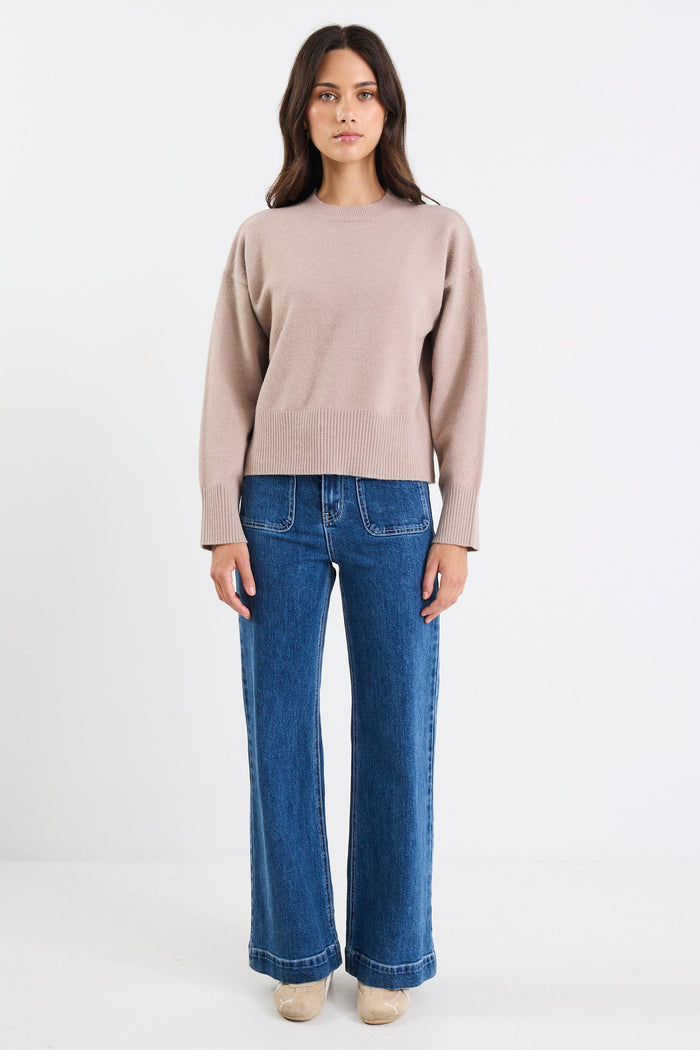 Woman wearing a beige sweater and blue jeans on a white background