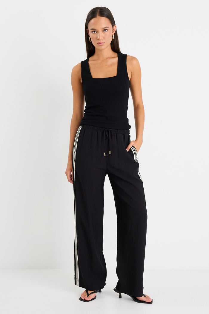 Woman wearing black pants with a side stripe and a black tank top