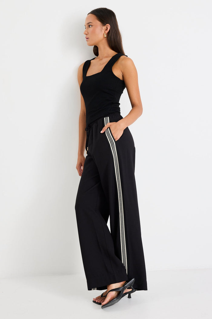 Woman wearing black pants with a side stripe and a black tank top
