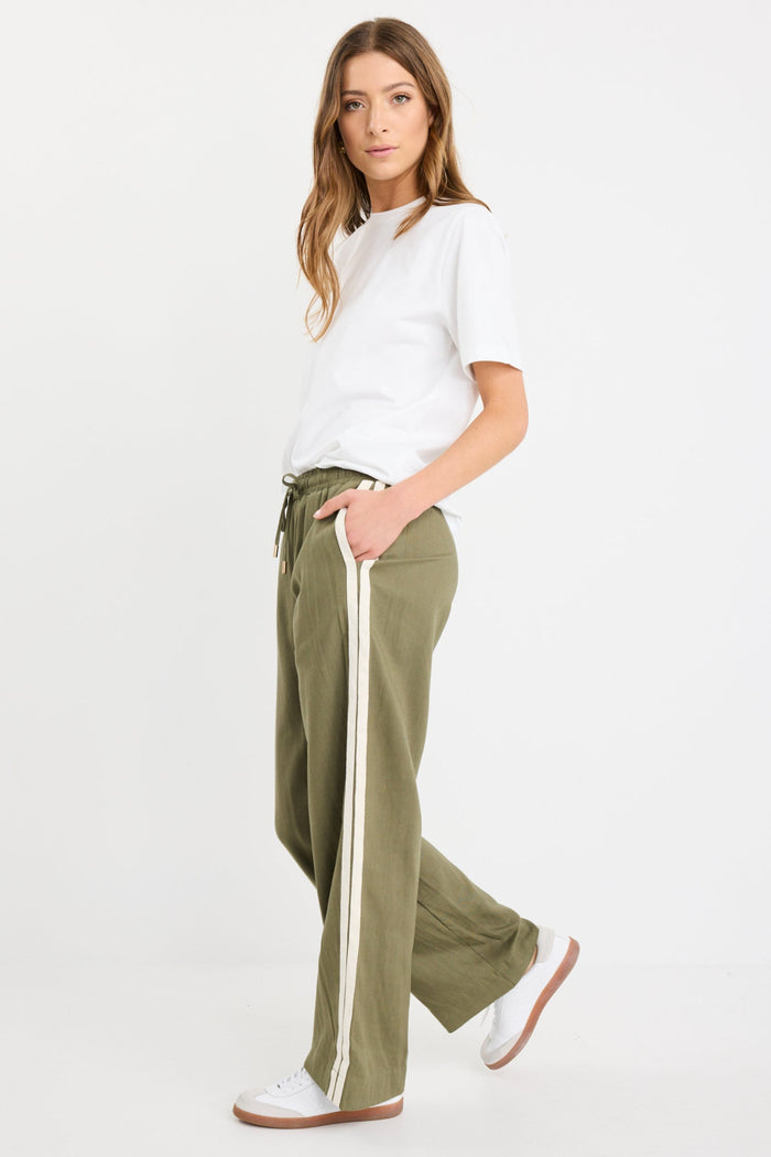 Woman wearing khaki wide-leg drawstring pants with an elastic waist, featuring a relaxed fit and side stripe detail, styled with a plain white tee and white sneakers.