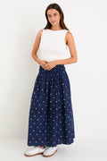 Woman wearing a white top and navy skirt with white patterns on a white background