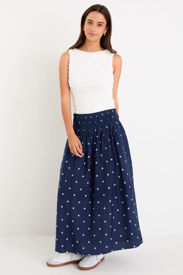 Model wearing a navy polka dot maxi skirt with a shirred elastic waist and a flowy silhouette.