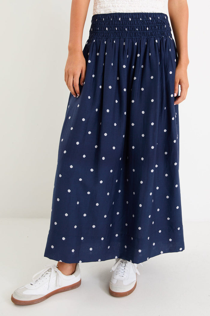 Model wearing a navy polka dot maxi skirt with a shirred elastic waist and a flowy silhouette.