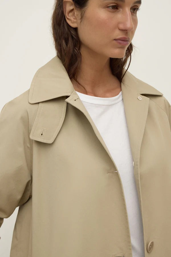 Person wearing a beige trench coat over a white shirt on a plain background