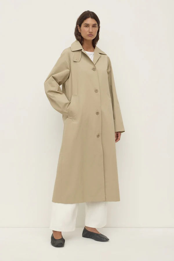 Person wearing a beige trench coat on a white background