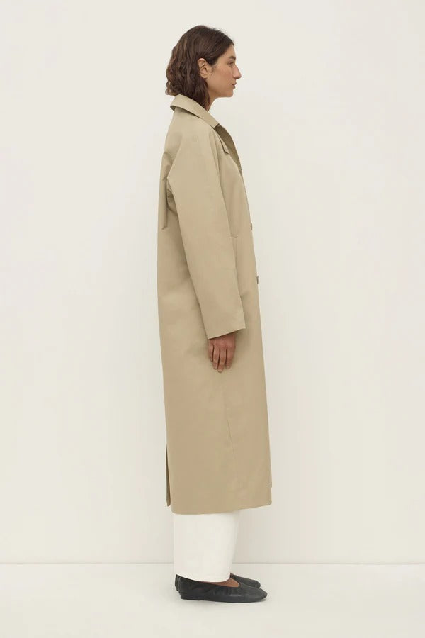 Person wearing a beige trench coat on a white background