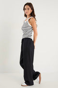 Woman wearing black wide-leg linen pants with an elasticated waistband, styled with a black and white striped tank and white sneakers.