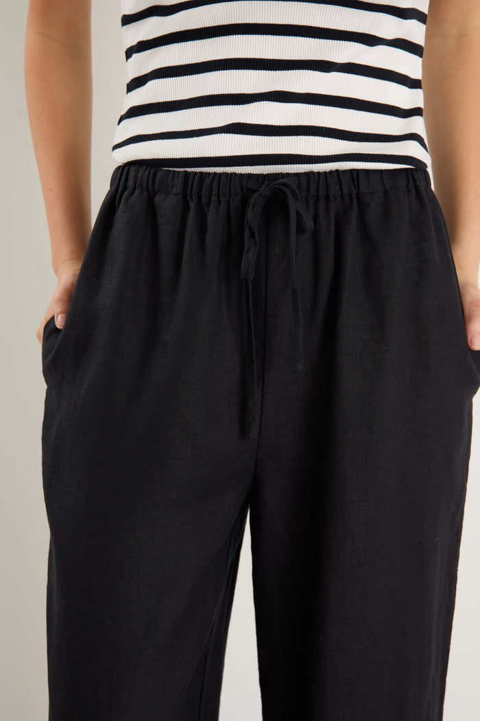 Woman wearing black wide-leg linen pants with an elasticated waistband, styled with a black and white striped tank and white sneakers.