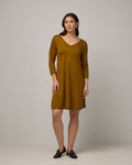 Model wearing Willow Swing Dress in Spiced Pear, a dark mustard color. Willow Swing Dress is a merino wool long sleeve, v-neck, knee length swing dress with pockets available in sizes XS-3X Regular, XS-3X Long.