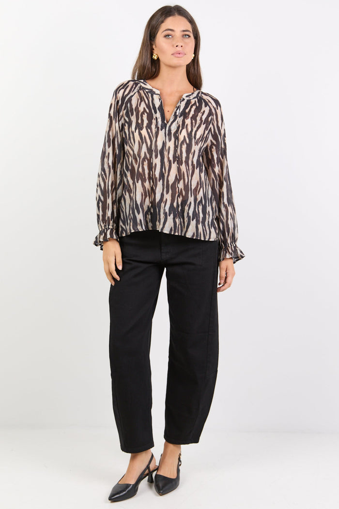 Woman wearing a patterned blouse and black pants on a white background
