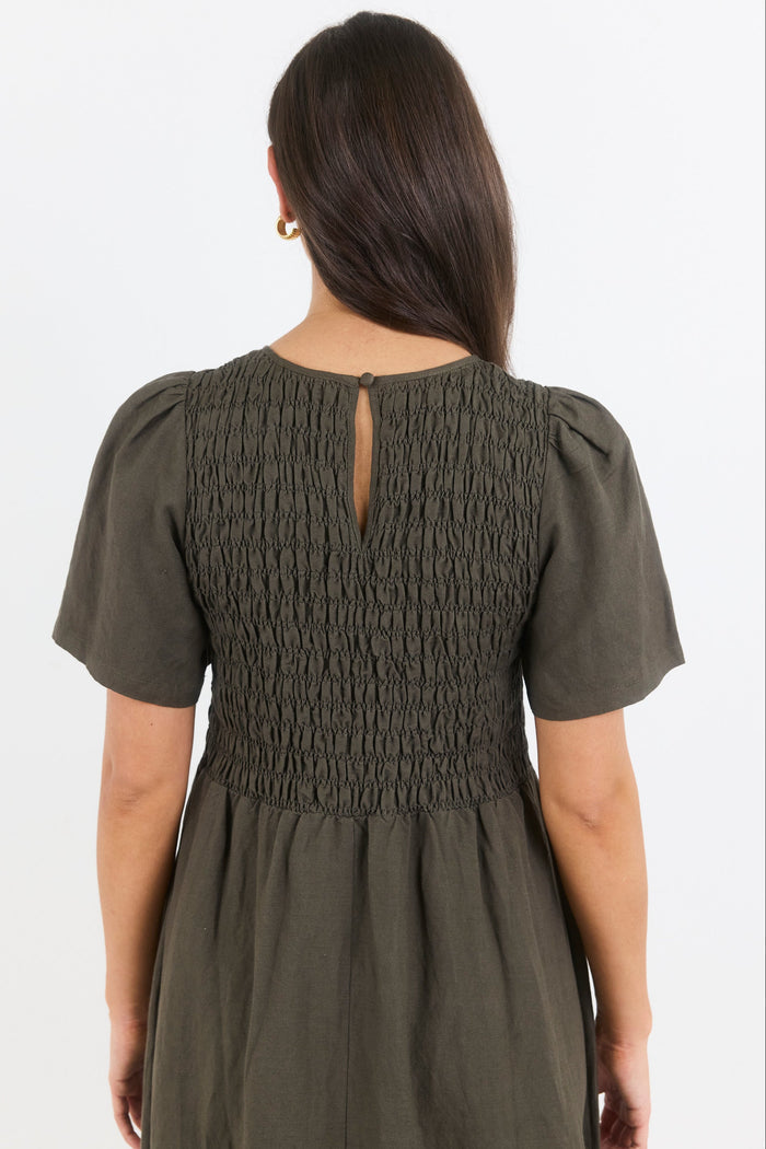 Woman wearing an olive green dress with smocked bodice on a white background
