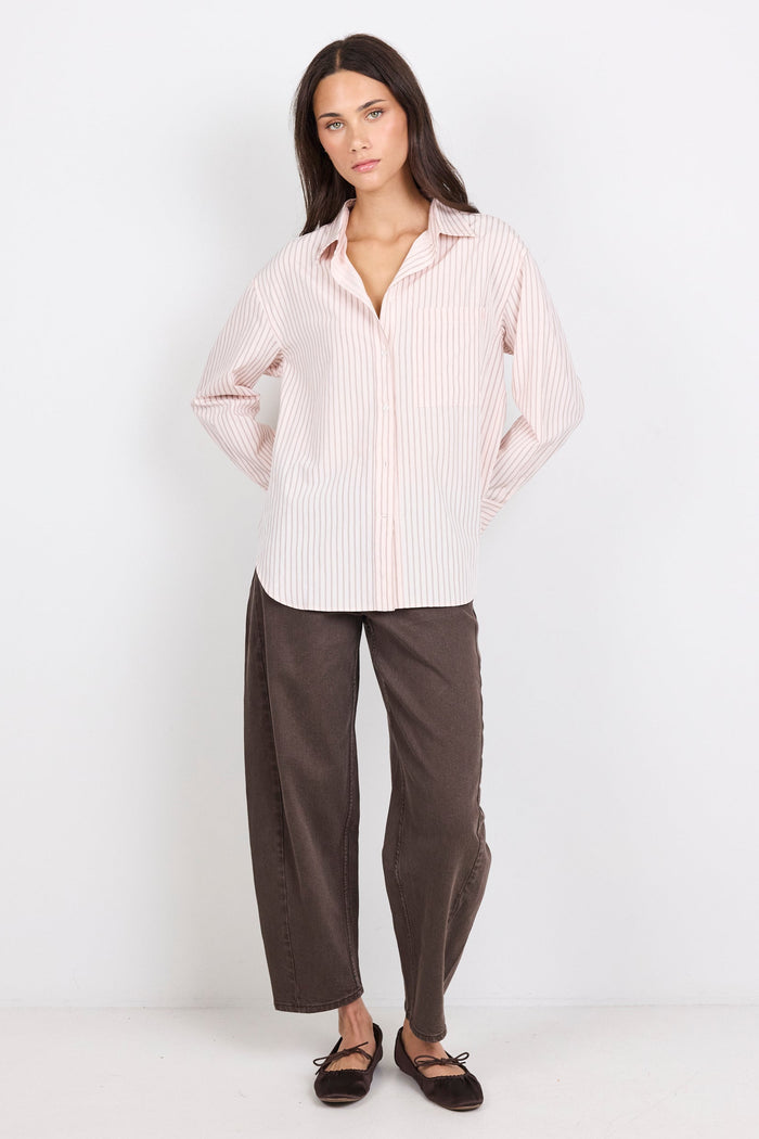 Woman wearing a light pink striped shirt and brown pants on a white background