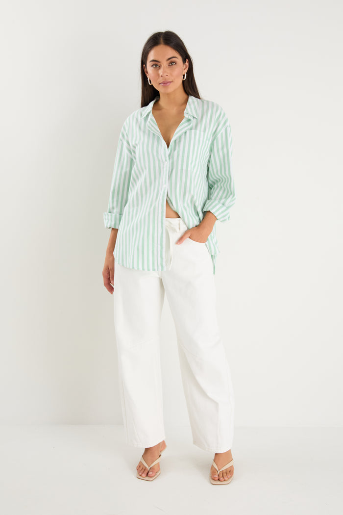 Woman wearing a light green striped shirt and white pants on a white background