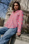 Woman in a red and white striped shirt and blue jeans sitting in front of a cathedral.
