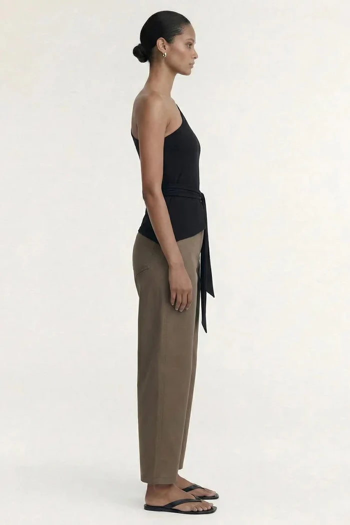 A model shown in profile wearing a black halter top with a side tie, beige wide-leg trousers, and black flip-flops against a plain off-white studio background.
