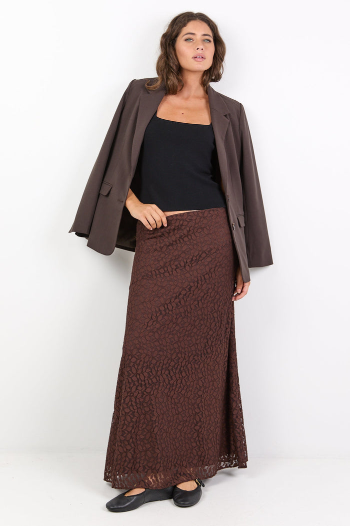 Woman wearing a brown coat, black top, and patterned skirt on a white background