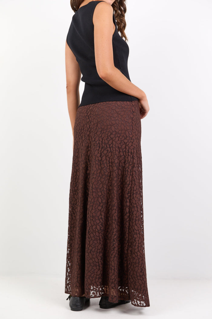 Person wearing a black sleeveless top and brown patterned skirt on a white background