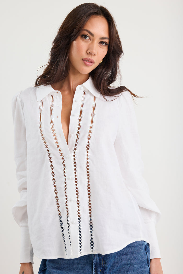 Woman wearing a white blouse with decorative stitching on a plain background