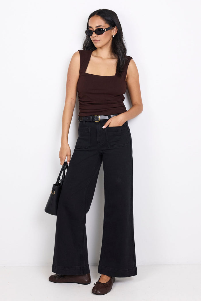 Woman wearing a brown top and black wide-leg pants holding a black handbag on a white background