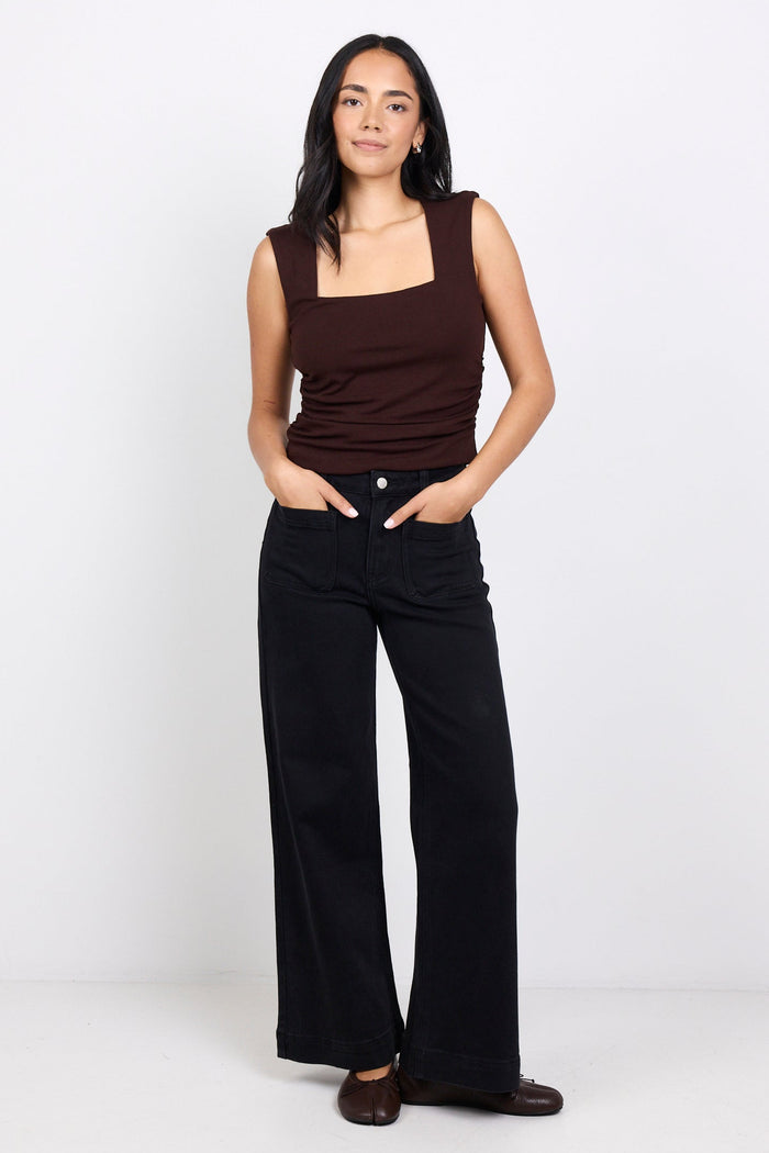 Woman wearing a brown sleeveless top and black pants on a white background