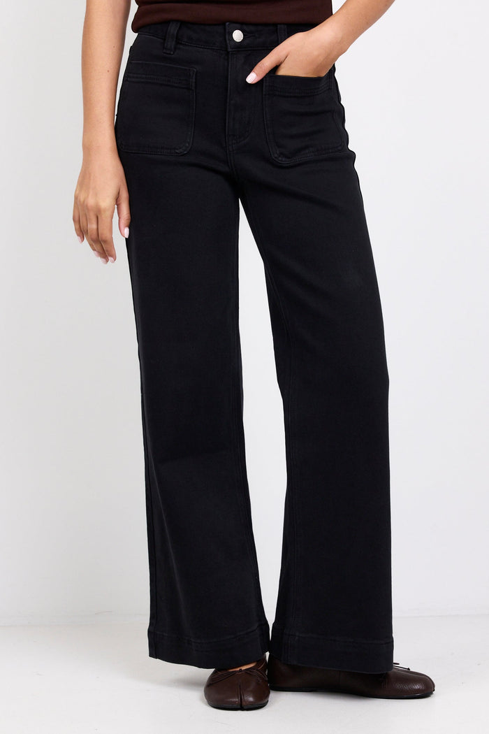 Person wearing black flared jeans and a brown top on a white background