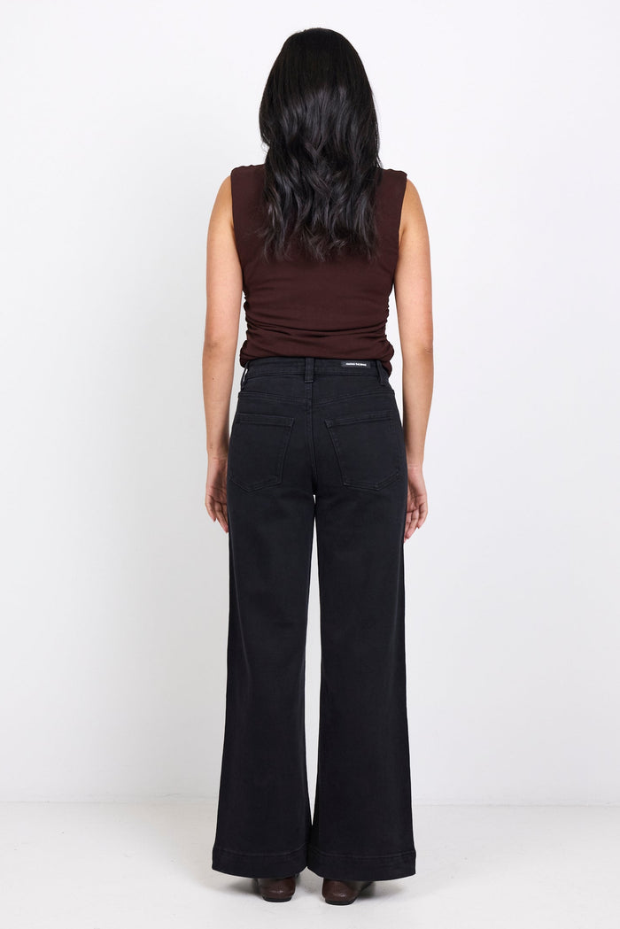 Person wearing a brown sleeveless top and black wide-leg pants on a white background