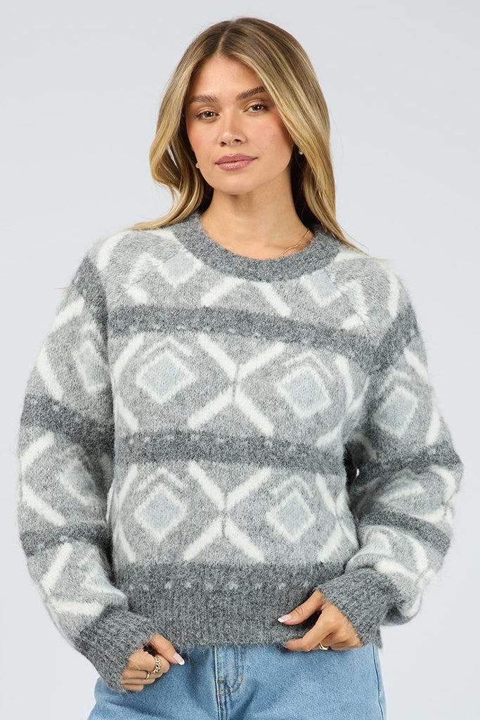 Person wearing a patterned sweater and blue jeans on a white background