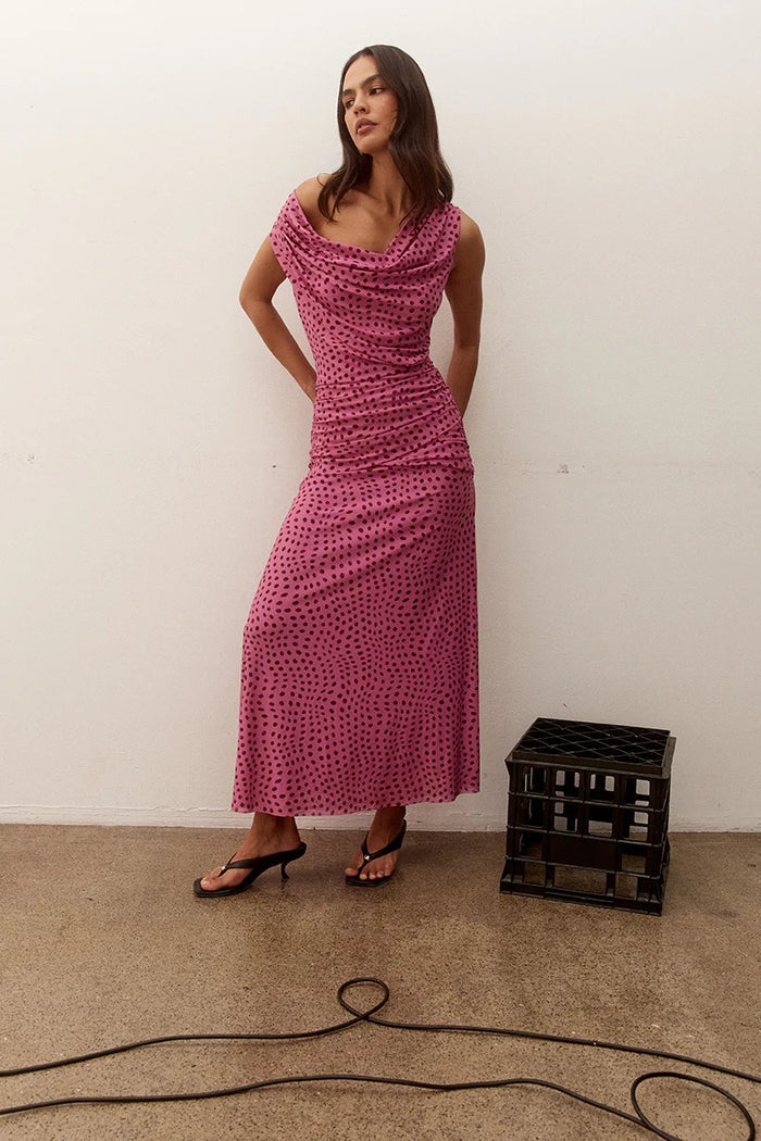 Woman wearing a pink dress standing next to a black crate against a white wall.